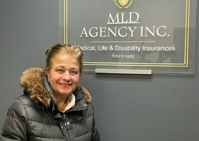 Excited woman (veteran) holding paperwork in front of MLD Agency sign