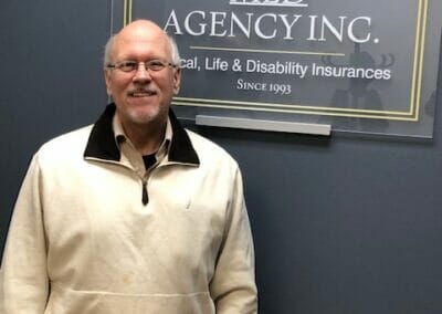 Smiling Medicare Advantage Plan cutsomer in front of MLD sign happy to have enrolled in an MAPD plan