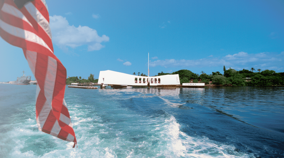 View of the Pearl Harbor Arizona Memorial with an American flag in the foreground.