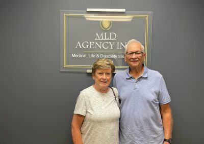 A happy couple standing in front of the MLD sign after saving money on their car and home insurance through MLD Agency, Inc. in St. Charles, Illinois.